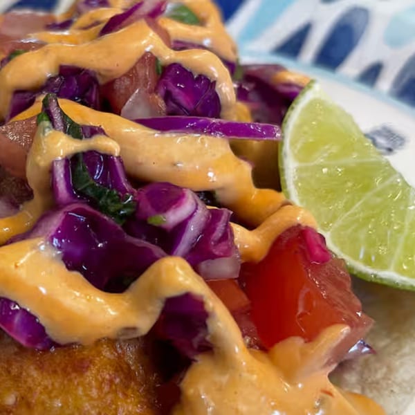 Close-up of a Mexican taco with fried fish, purple cabbage, red salsa, and creamy orange sauce.