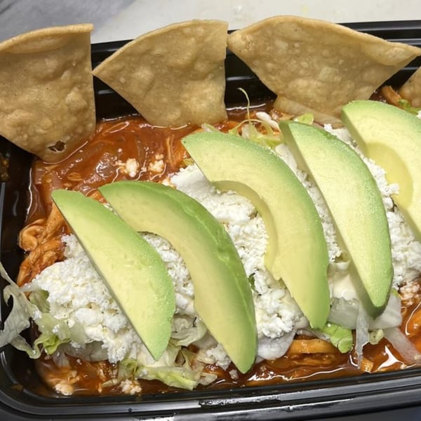 Mexican chilaquiles with red sauce, shredded chicken, crumbled cheese, avocado slices, and tortilla chips.