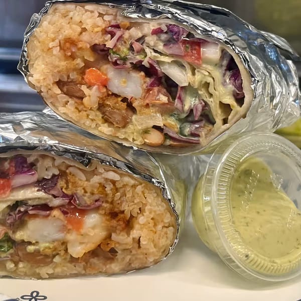Two halves of a shrimp burrito, wrapped in foil, with a side of green sauce.