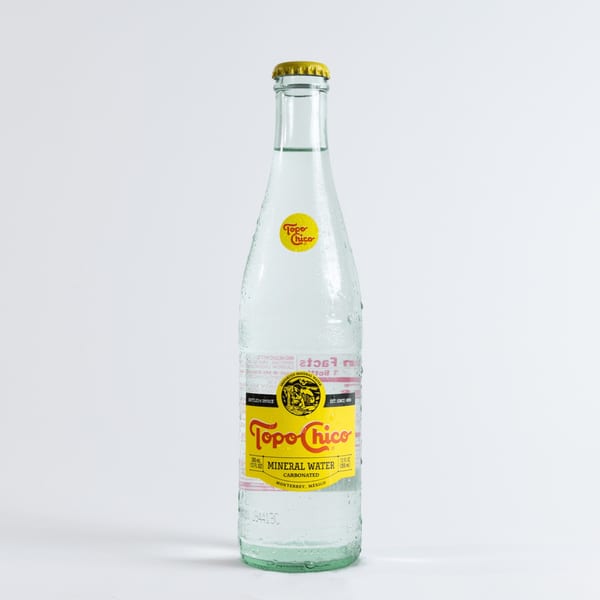 A cold, condensation-covered bottle of Topo Chico mineral water with a yellow label and cap.