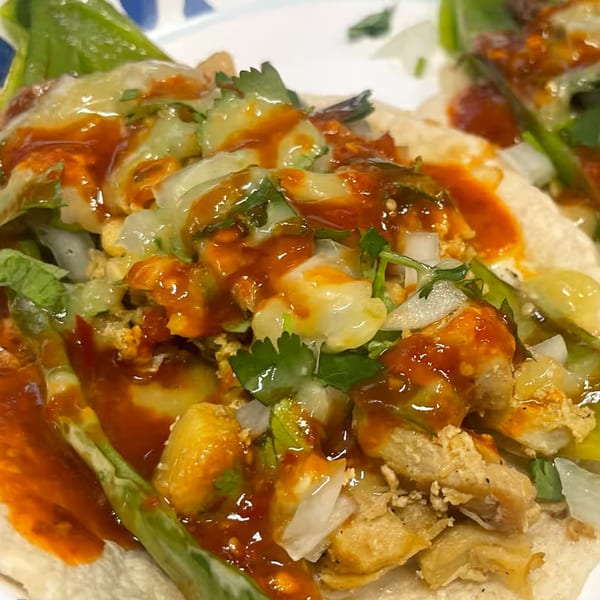 Close-up of a Real Taco with chicken, onions, cilantro, and red sauce on a corn tortilla.