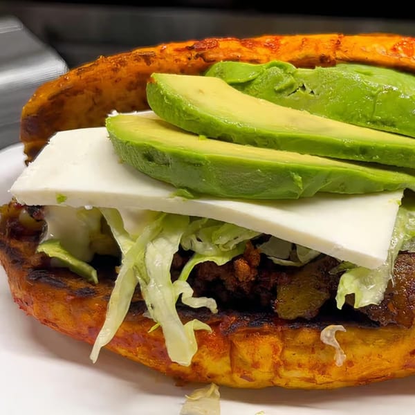 A Mexican gordita with avocado slices, white cheese, shredded lettuce, and meat filling.
